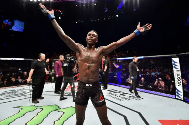 Israel Adesanya opens his arms wide in celebration