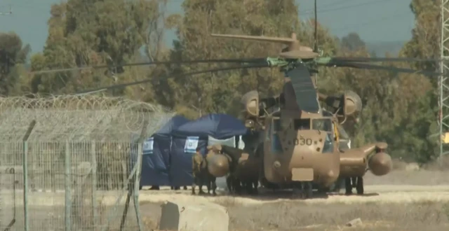 A military helicopter with two tents behind it and a barbed wire fence next to it