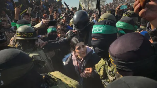 Huge crowds and masked Hamas fighters surround Israeli woman Arbel Yehud in the middle of image