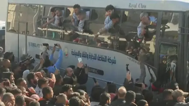 Palestinian prisoners hanging out of windows of a bus with large crowds waving to them