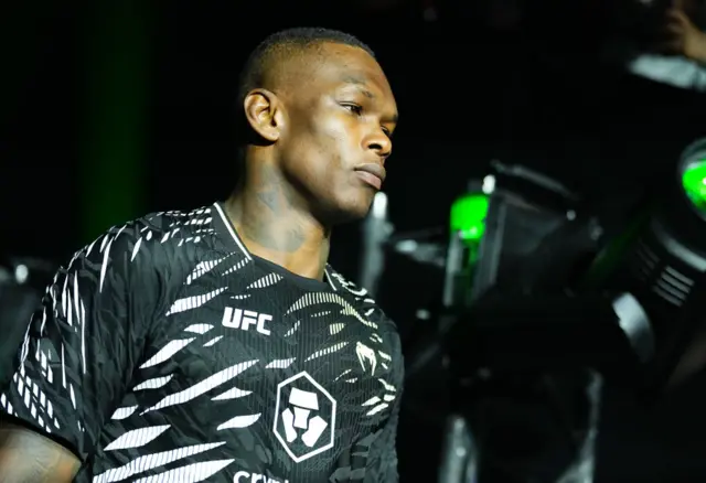 Israel Adesanya dressed in black makes his walk to the octagon