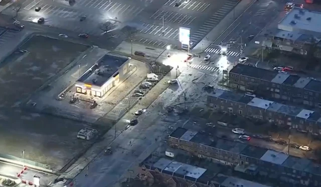 A birds eye view of a neighbourhood where lots of debris and stationary cars are seen next to a car park and houses