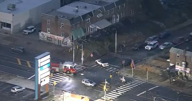 A birds eye view of a neighbourhood where lots of debris and stationary cars and a firetruck are seen next to a car park and houses