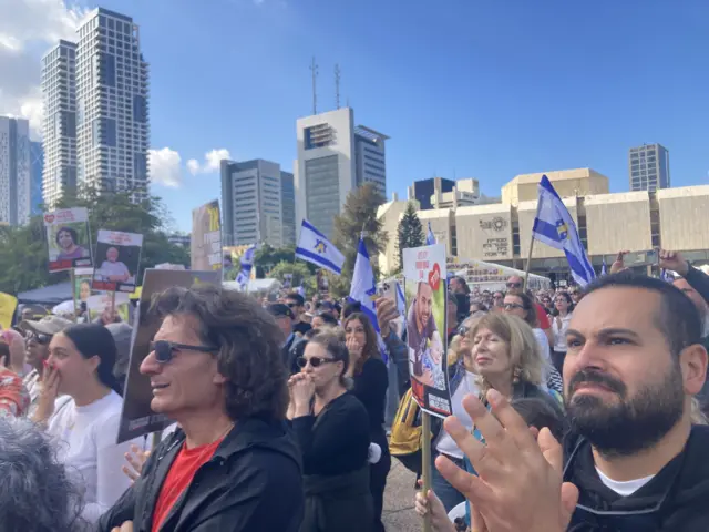 A crowd of people holding Israeli flags and banners clap and smile