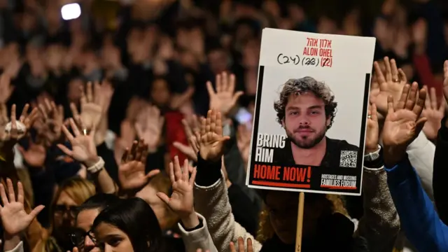 Protesters in Tel Aviv hold hands up and sign picturing Alon Ohel, which says "bring him home now"