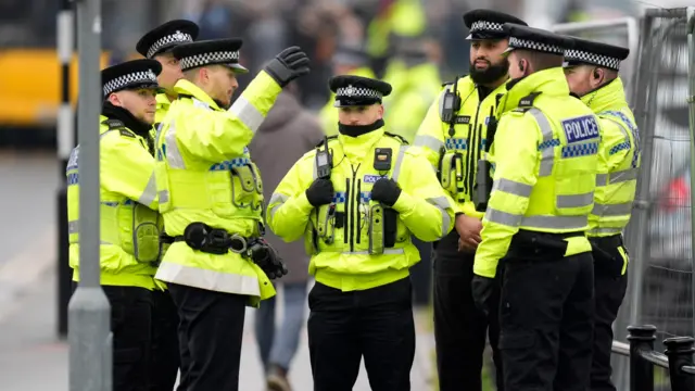 Police in yellow jackets and black hats stood in front of a railing