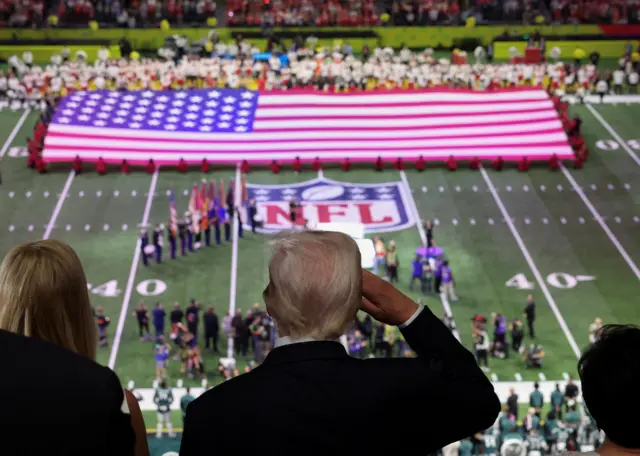 President Donald Trump salutes as the national anthem is sung by Jon Batiste