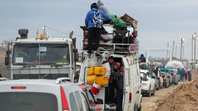 A queue of cars and trucks wait to pass through a checkpoint, run by US and Egyptian security contractors; Palestinians are crammed into one white van with some on the roof.