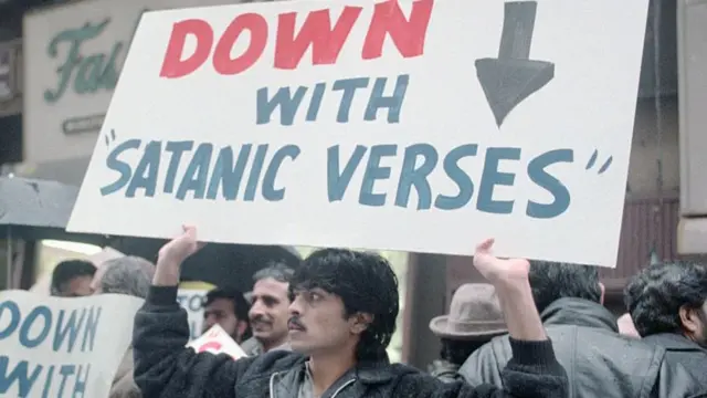 A man holds a sign above his head reading: "down with Satanic verses"