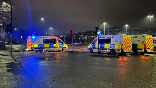 Three police vans and police tape near the flats.