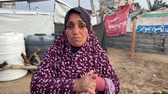 Samira al-Sabea looking into camera with hands crossed, with wall and building in background