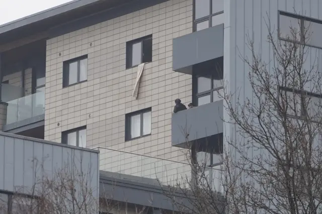 Armed police on a balcony, with a towel hanging out a nearby open window.