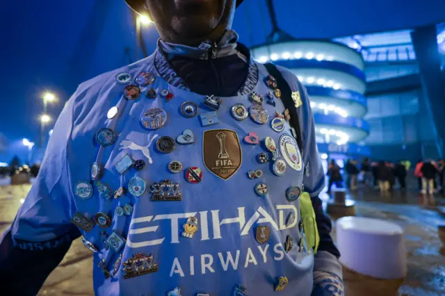 Man City fan with pin badges on his shirt arrives at Etihad Stadium