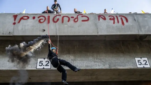 A protester jumps from a bridge as demonstrators gather on the highway to demand the hostage swap continue in Tel Aviv