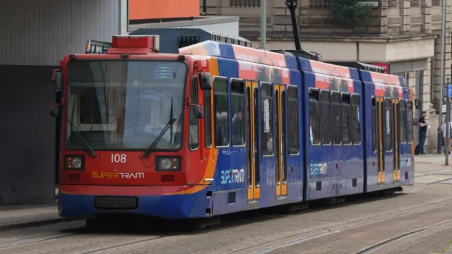 A blue and red trams runs down a city street. It has the number 108 beneath the main windscreen