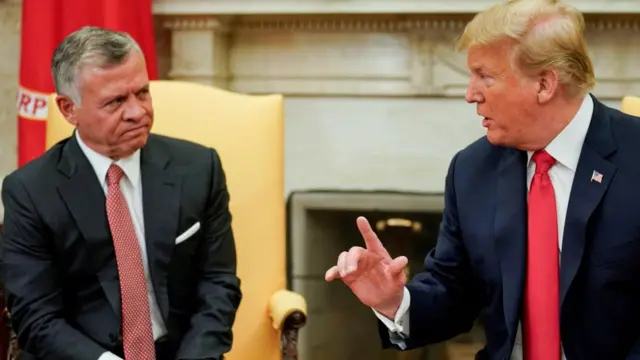 Jordanian King Abdullah and Donald Trump sat on yellow chairs with fire place behind, looking at each other in conversation.