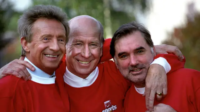 Denis Law, Bobby Charlton and George Best smiling together.