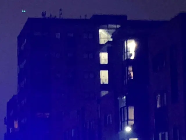 A large apartment block in the dark except for a line of windows lit up