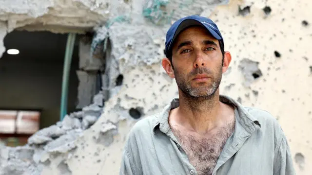 Gili Roman in grey shirt with crumbling building behind him