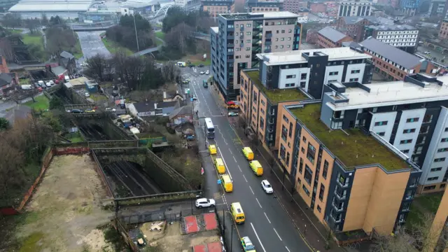 Emergency vehicles parked on a street lined with apartment blocks, viewed from above