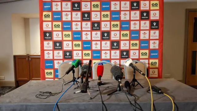 Desk with microphones on in front of backdrop