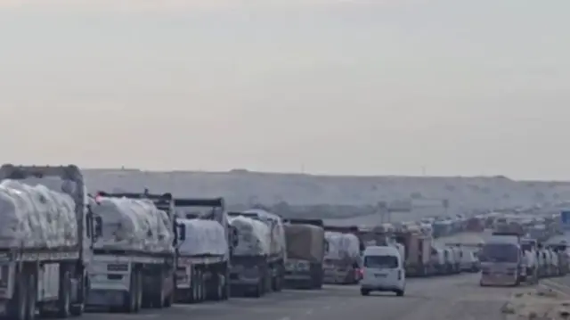 A road stretching into the distance, lined on both sides by trucks with goods loaded on them as far as the eye can see