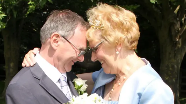 Elaine and Eric Hunter on their wedding day. Their heads are touching and they have their arms around each other, smiling.