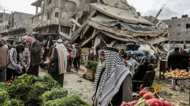 Palestinian residents, shopping at the market, try to meet their basic needs among the collapsed buildings as they continue to live in Khan Yunis, Gaza, which was heavily damaged by Israeli airstrikes before their withdrawal, on February 12, 2025