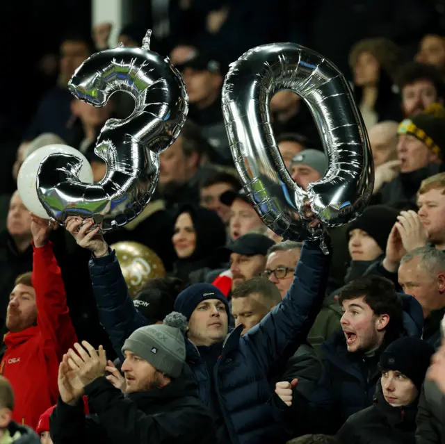 Fans hold up 30 balloons in the away end