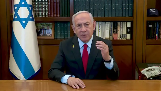 Benjamin Netanyahu speaking at a desk in front of a wooden bookshelf and the Israeli flag