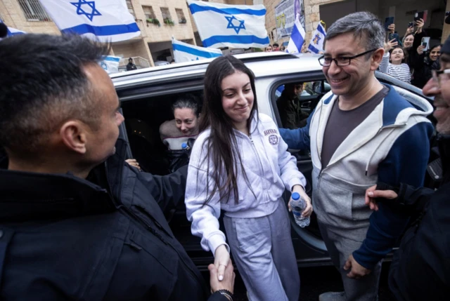 Karina Ariev leaving a car in a grey tracksuit with Israeli flags in the background