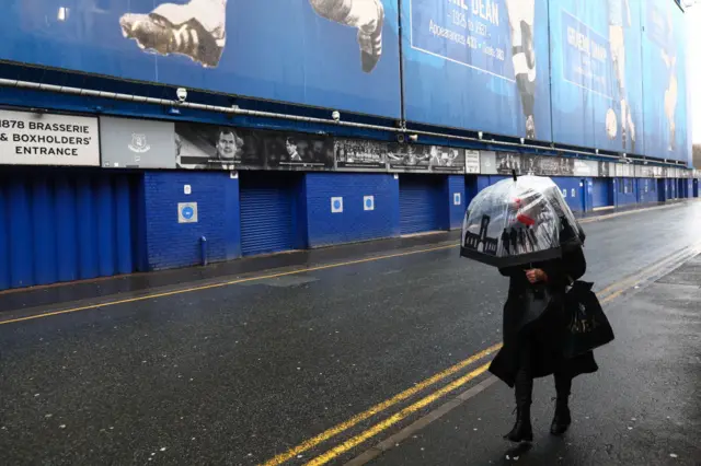 A fan with an umbrella walks by Goodison Park during Storm Darragh