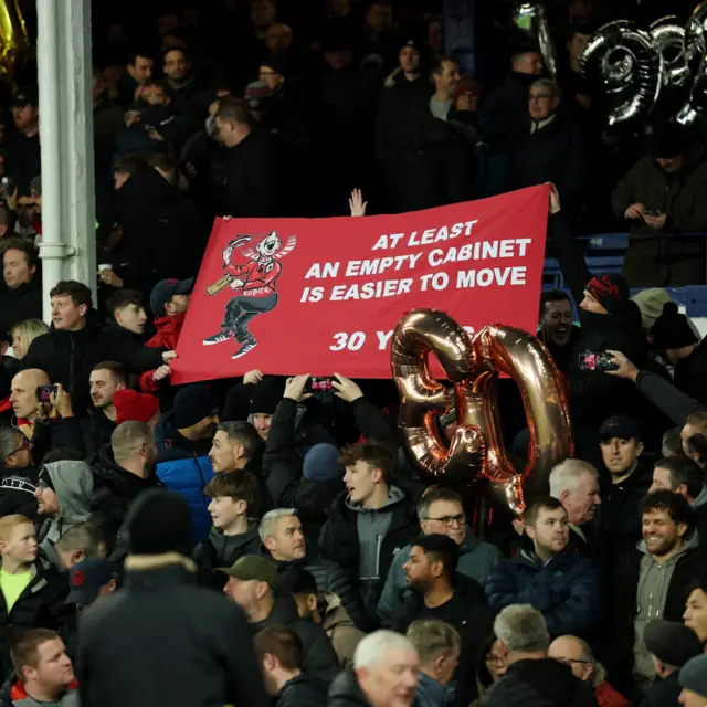 Liverpool fans hold up a banner reading - 'An empty cabinet is easier to move'