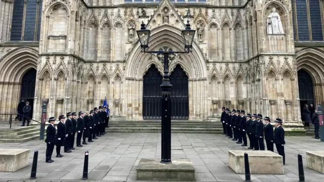 Police officers in black uniforms line either side of the door to York Minster