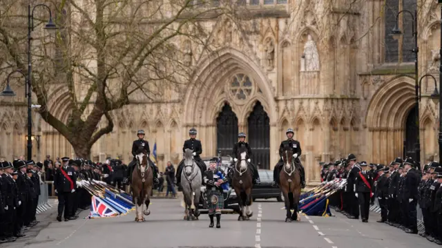 Procession leaves York Minster, led by man with bagpipes and four horses