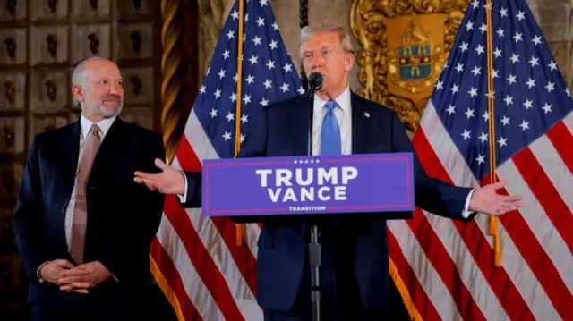 Trump stands at a campaign podium with Howard Lutnick to his right