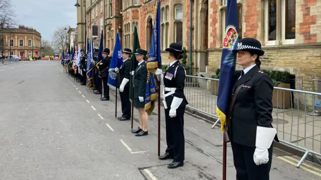 Police officers holding flags stand along a road