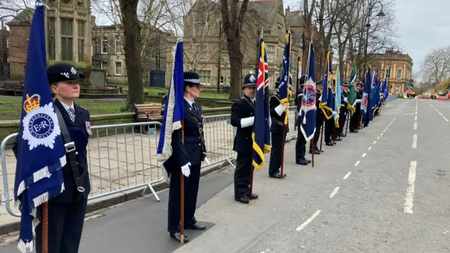 Police officers holding flags stand along a road