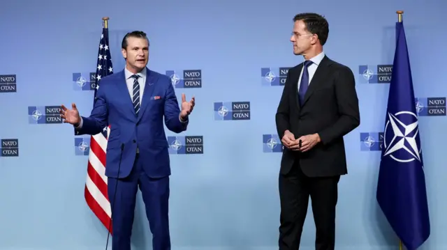 Pete Hegseth standing up and speaking while Mark Rutte looks on