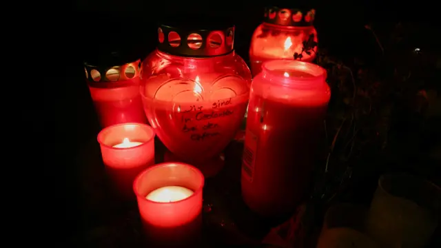 Candles are lit at the makeshift memorial scene, one inscribed with the message "Our thoughts are with you"