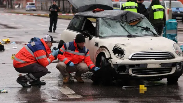 Police takes pictures of the white mini cooper used in the attack. they are wearing high-vis vests and the car is heavily damaged, with its roof dented.