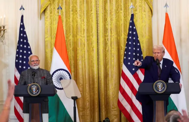 Two men stand at podiums while the man on the right points at raised hands