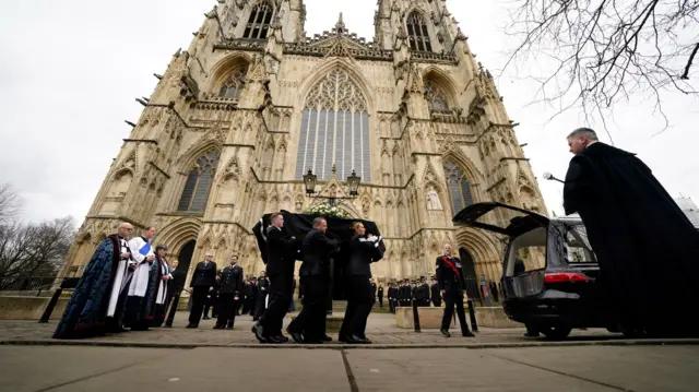 Coffin is carried into car by pallbearers