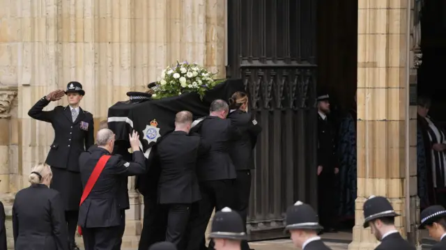 Pallbearers bring the coffin, covered in white flowers, into York Minster as officers salute.