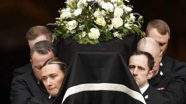 The coffin of PC Rosie Prior, draped in black with white flowers on, is carried out of York Minster after her funeral.