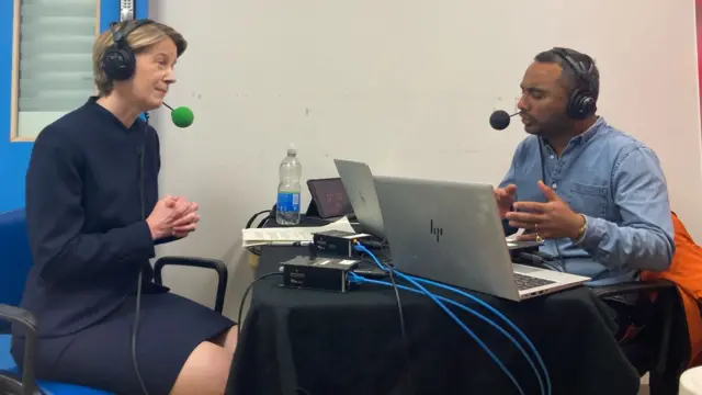 Pritchard, left, sits at a small round table laden with radio equipment, speaking to Amol Rajan on the right