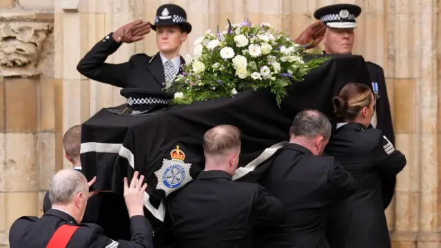 Pallbearers bring the coffin, covered in white flowers, into York Minster as officers salute.