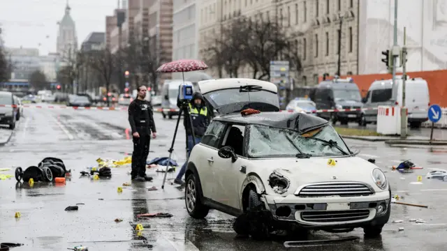 Police examine the wreck of the white Mini cooper that was at the scene of the attack. The bonnet is severely dented, the winscreen is cracked and front window shattered.