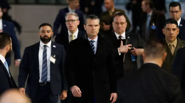 Pete Hegseth wearing suit walking with group of men walking behind him