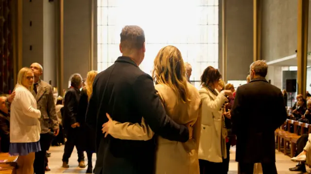 A man and a woman with their backs to the camera with their arms around each other in front of a bright window